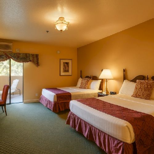 A cozy hotel room with two double beds, warm yellow walls, a desk and chair by a sliding door, and soft lamps casting a inviting glow.