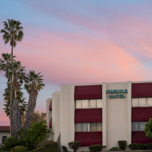 Palm trees, a red and white building, and a pink-orange sky at sunset.