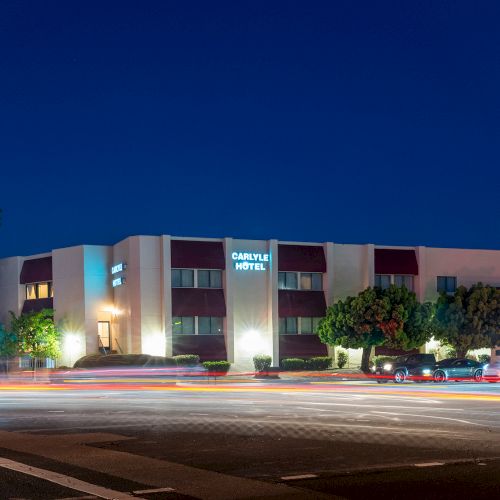 A small modern motel at dusk with a row of parked cars along the street and palm trees silhouetted against a deep blue sky.