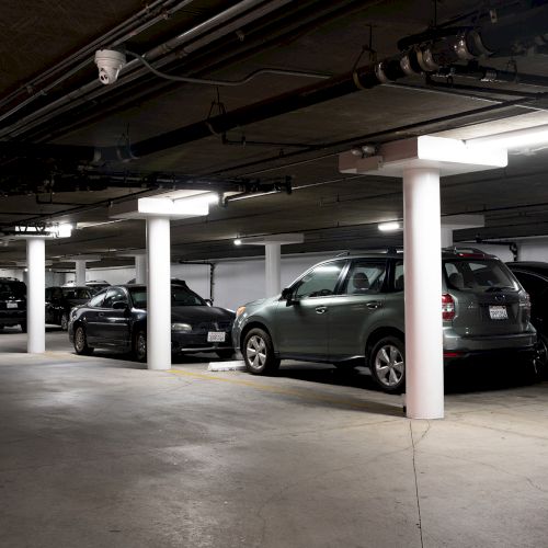 An empty, well-lit underground parking garage with cars parked along pillars and concrete floors.