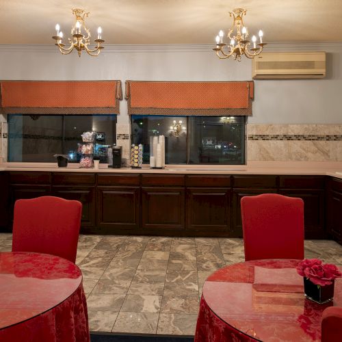 A cozy living room with red chairs, a stone fireplace, warm lighting, and a flat-screen TV above a wooden mantel.