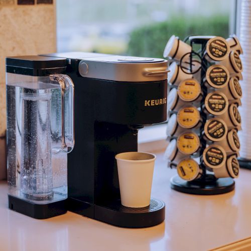 A close-up of a kitchen counter with a coffee maker, a canister of cookies, and a cup, with a blurred window view in the background.
