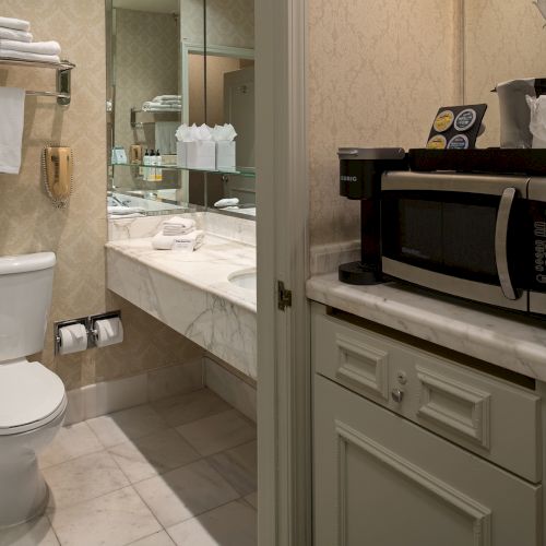 A small bathroom with a toilet, a sink, and a narrow wooden cabinet; a mirror and towel rack reflect warm, cozy lighting.