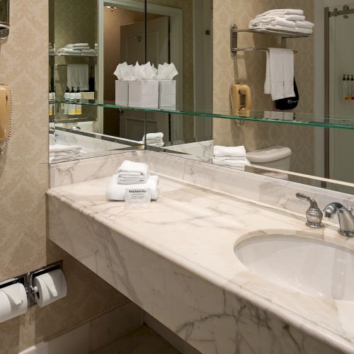 A public restroom or hotel bathroom with a double sink vanity, framed mirror, and beige-tiled walls and countertop.