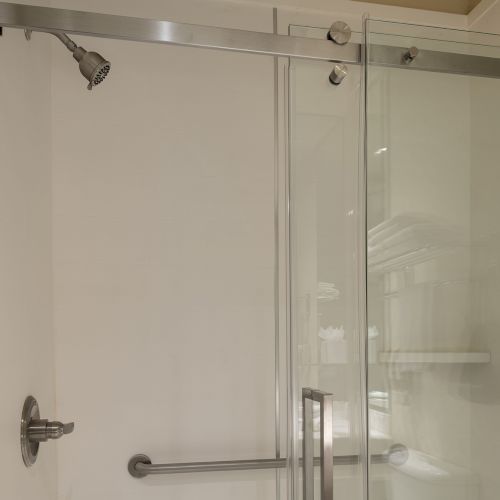 A shower with a glass door, white wall tiles, a chrome towel bar, and a small soap dish; ceiling light visible.