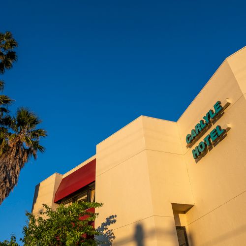 A tan building with curved stucco walls and a red tile roof, accented by a clear blue sky and a palm tree silhouette in the foreground.