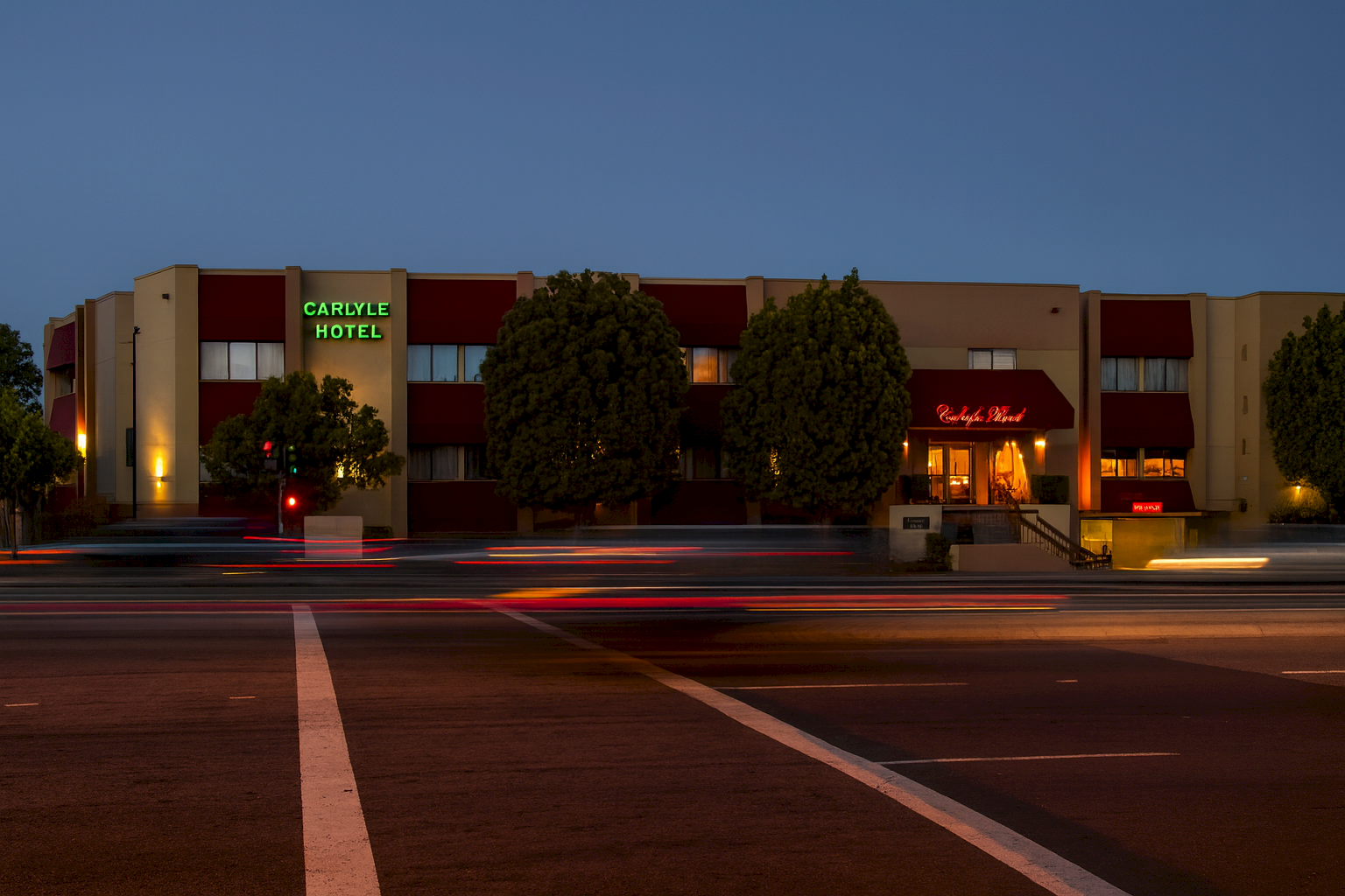Exterior of Carlyle Hotel at dusk with moving traffic light streaks on a road.