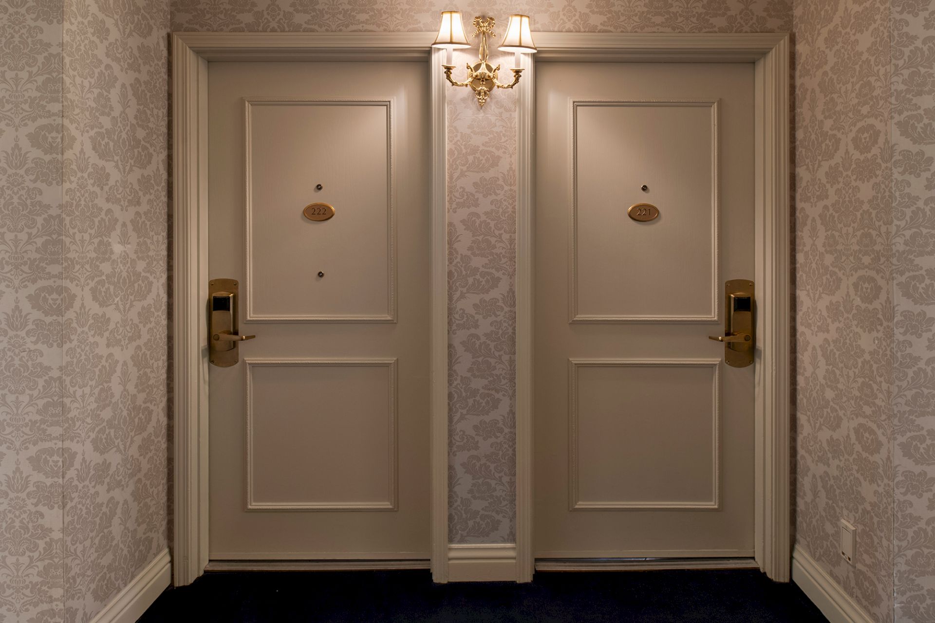 Ornate double doors with brass numbers 222 and 221, gold chandelier-style light above, in a patterned hallway.