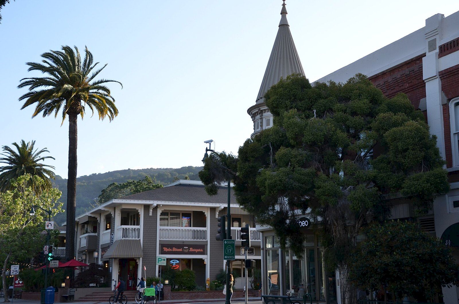 Palm trees and a brick church with a tall spire rise above a city street with buildings and traffic signs.